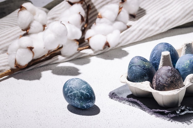 Huevos de pascua azules teñidos con té de hibisco en un cartón de huevos sobre un fondo de hormigón blanco