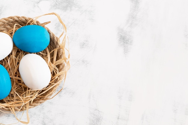 Los huevos de Pascua blancos y azules yacen en una bandeja hecha de hilo debajo de ellos hay heno