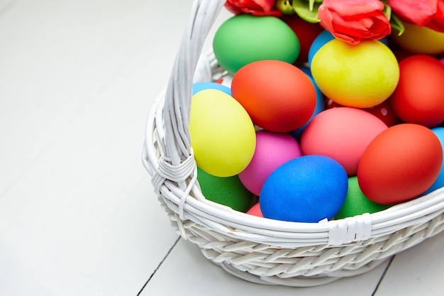 Huevos de Pascua en canasta de mimbre y flores de tulipán rojo sobre mesa de madera blanca