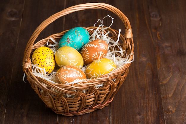 Huevos de Pascua en cesta sobre fondo de madera oscura