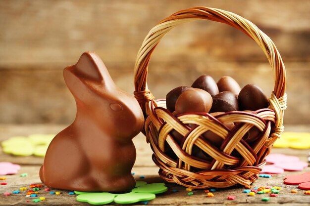 Huevos de Pascua de chocolate en cesta de mimbre y conejo de chocolate sobre fondo de madera