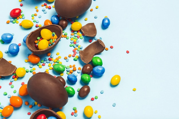 Huevos de Pascua de chocolate rotos y enteros, dulces multicolores sobre fondo azul. Concepto de celebración de Pascua, decoraciones de Pascua, búsqueda de dulces para Conejito de Pascua. Vista plana, vista superior. Copia espacio.