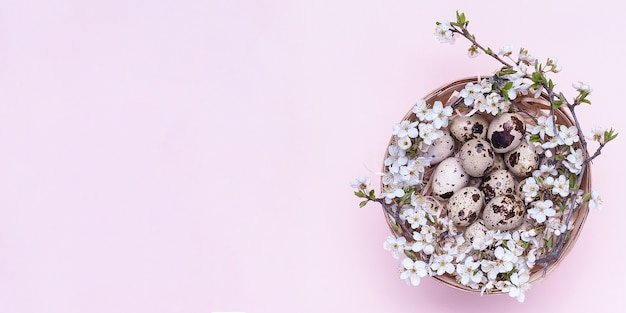 Huevos de pascua de codorniz en una canasta con flores sobre un fondo rosa.