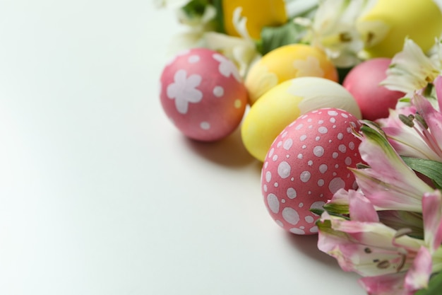 Huevos de Pascua de color y flores de alstroemeria sobre fondo blanco.