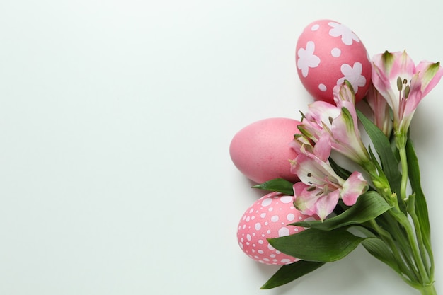 Huevos de Pascua de color y flores de alstroemeria sobre fondo blanco.