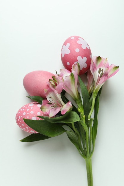 Huevos de Pascua de color y flores de alstroemeria sobre fondo blanco.