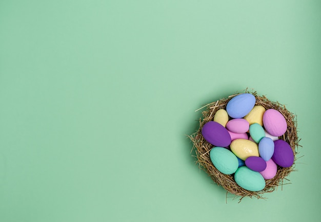 Huevos de Pascua coloreados en un nido decorativo de paja sobre un fondo verde, espacio de copia, plano