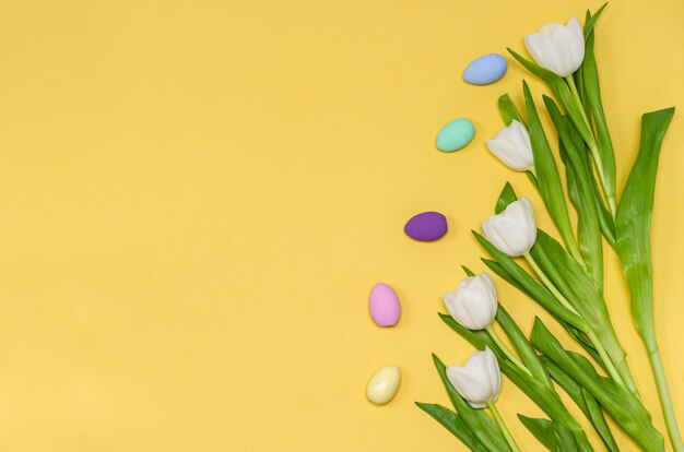 Huevos de Pascua coloreados con un ramo de tulipanes blancos sobre un fondo amarillo, espacio de copia,