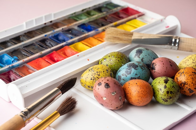 Huevos de Pascua para colorear. Pintura, pinceles, huevos de codorniz sobre un fondo rosa. Preparación para la celebración de la Pascua, decoraciones para la fiesta, fondo. Concepto creativo.