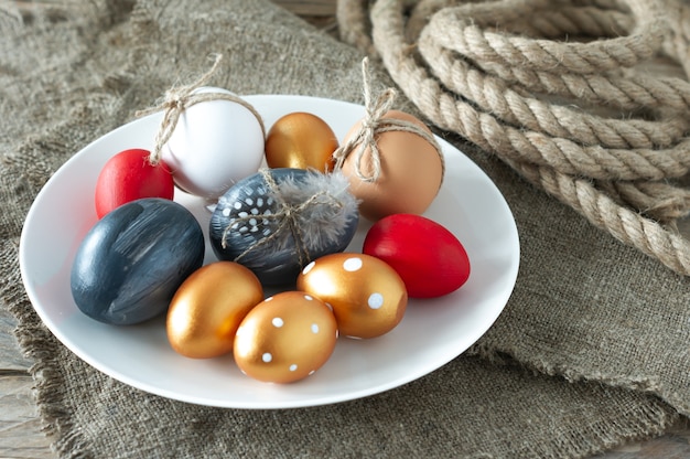 Huevos de Pascua de colores de moda, lienzos y cuerdas y plumas en un plato sobre la mesa de madera. Preparación para las vacaciones de semana santa. Composición festiva.