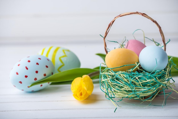 Huevos de Pascua coloridos y brillantes con tulipanes amarillos pintados a mano sobre un fondo blanco de madera Tarjeta de primavera festiva