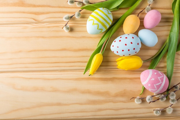 Huevos de Pascua coloridos y brillantes con tulipanes amarillos pintados a mano sobre un fondo de madera clara Tarjeta de primavera festiva