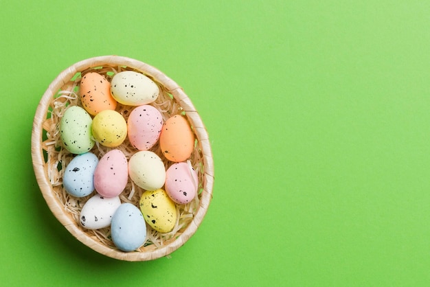 Huevos de Pascua coloridos en una canasta de mimbre contra un fondo coloreado vista superior de primer plano con espacio de copia