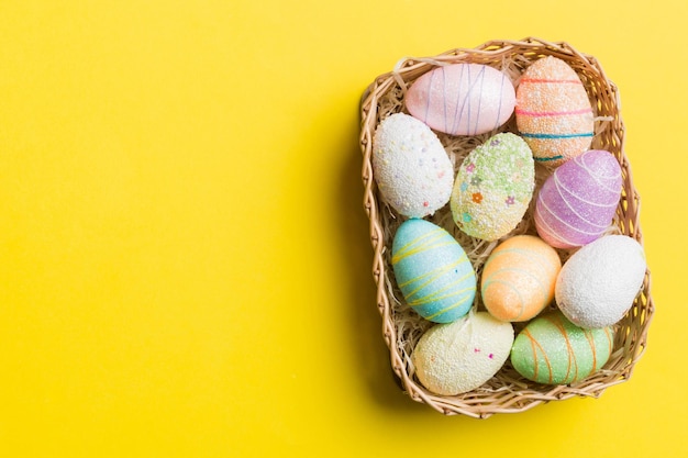 Huevos de Pascua coloridos en una canasta de mimbre contra un fondo coloreado vista superior de primer plano con espacio de copia