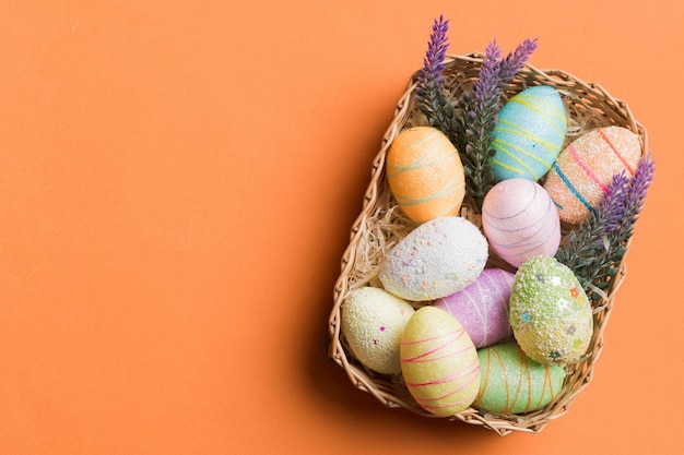 Huevos de Pascua coloridos en una canasta de mimbre contra un fondo coloreado vista superior de primer plano con espacio de copia