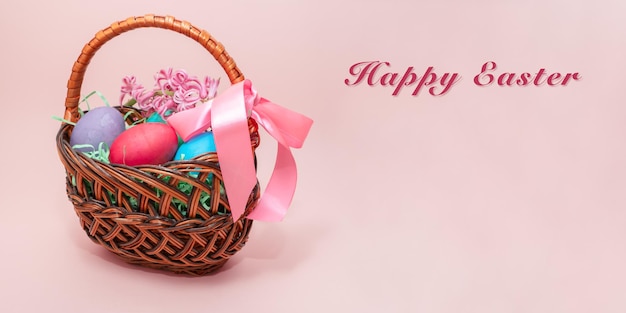 Huevos de Pascua coloridos en cesta de mimbre sobre fondo rosa.