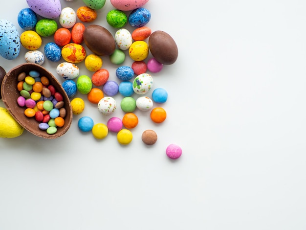 Huevos de pascua coloridos y de chocolate con grageas dulces sobre fondo blanco