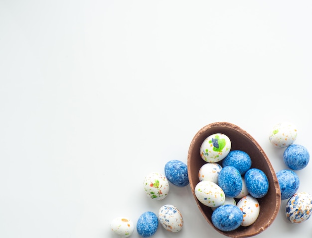 Huevos de pascua coloridos y de chocolate con grageas dulces sobre fondo blanco