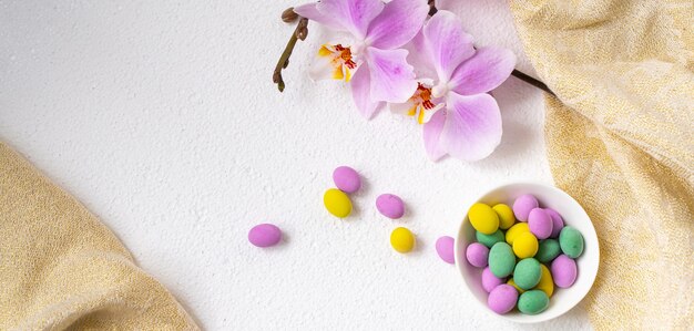 Huevos de Pascua coloridos y flor de la orquídea del phalaenopsis con la placa en el escritorio blanco.