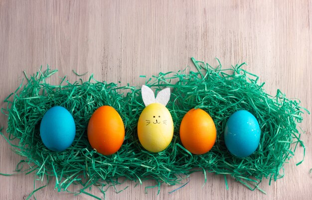 Huevos de pascua coloridos y huevo como un conejito de pascua en el medio, madera blanca. Concepto de pascua feliz.