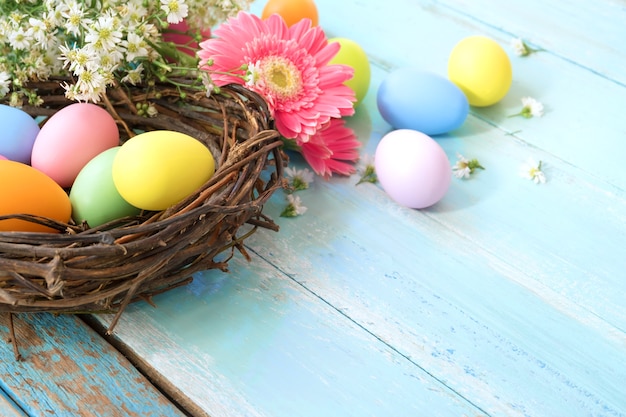 Huevos de Pascua coloridos en jerarquía con las flores en fondo de madera azul.