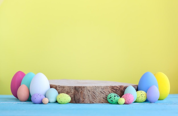 Huevos de Pascua coloridos con plataforma vacía de madera sobre fondo amarillo