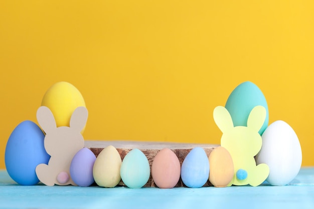 Huevos de Pascua coloridos con plataforma vacía de madera sobre fondo amarillo