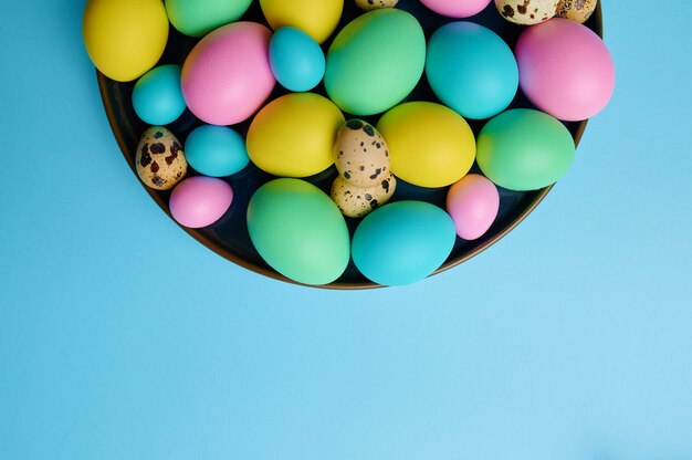 Huevos de Pascua coloridos en un tazón sobre la mesa azul, vista superior.