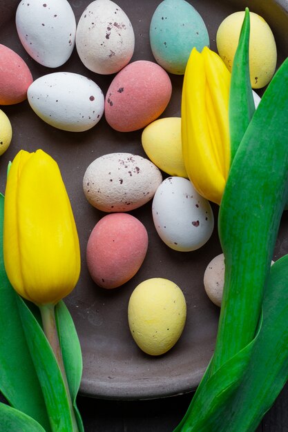Huevos de Pascua coloridos teñidos en una textura de fondo de madera vintage, diseño moderno de pasteles suaves con tulipanes amarillos