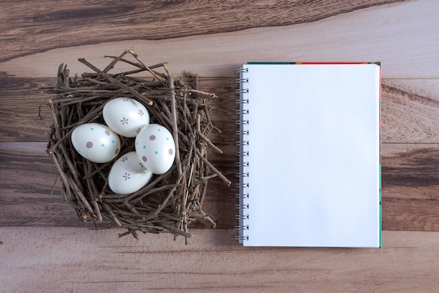 Huevos de Pascua decorados en un nido con ramas y un cuaderno en espiral sobre un fondo de madera