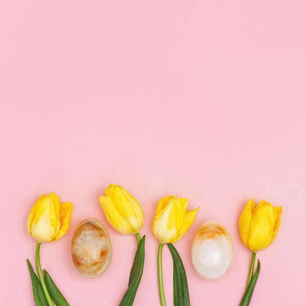 Huevos de Pascua decorativos y tulipanes de flores frescas amarillas de primavera sobre fondo rosa