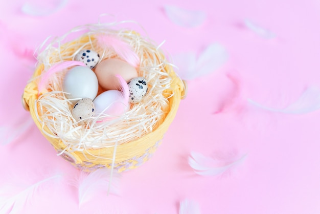 Huevos de Pascua de diferentes colores, huevos de codorniz y plumas blancas y rosadas sobre fondo rosa pastel, vista superior, endecha plana. Concepto de vacaciones de Pascua.