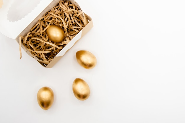 Huevos de Pascua dorados en una caja con estrellas doradas sobre fondo blanco