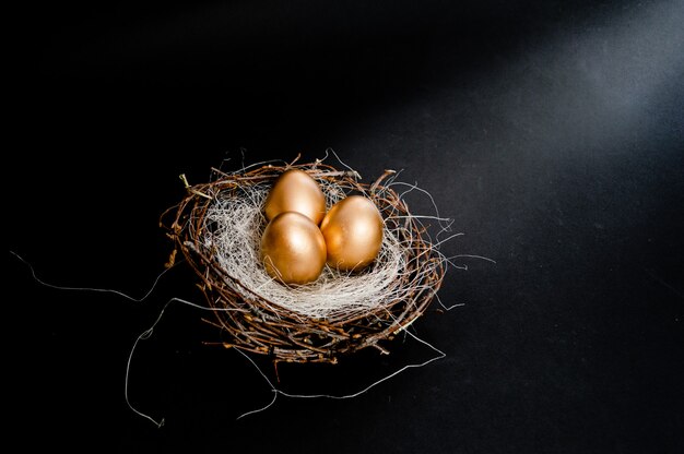 Huevos de Pascua dorados en nido de pájaros sobre fondo negro