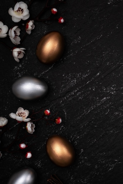 Huevos de Pascua dorados y plateados con flor de ciruelo en el fondo de la tabla de pizarra.