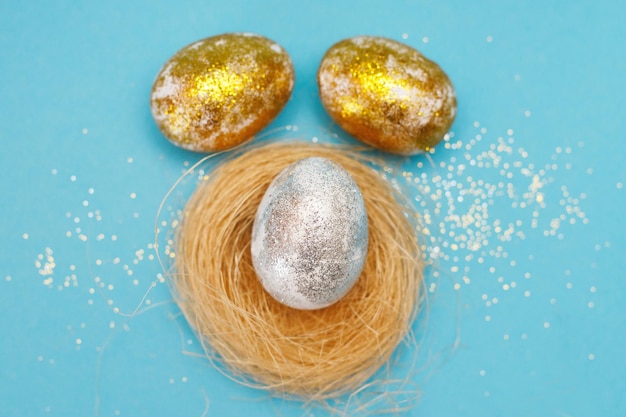 Huevos de Pascua dorados y plateados con nido sobre un fondo azul Concepto de Pascua Feliz Pascua Copiar espacio