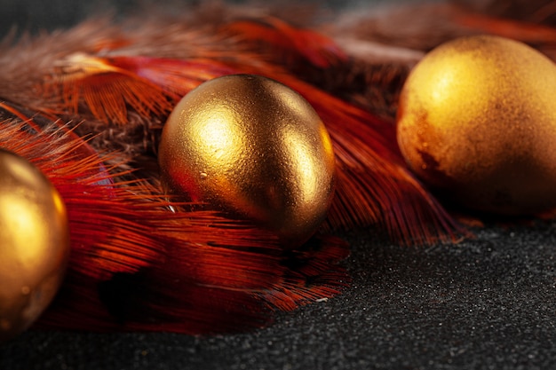 Huevos de Pascua dorados sobre plumas de pájaro rojo de cerca