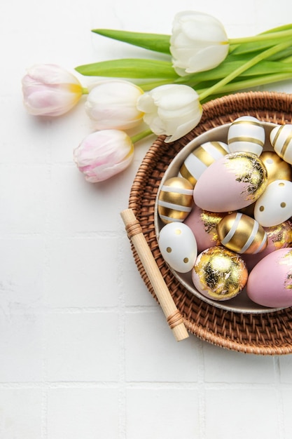 Huevos de Pascua dorados y tulipanes rosas sobre fondo de baldosas blancas