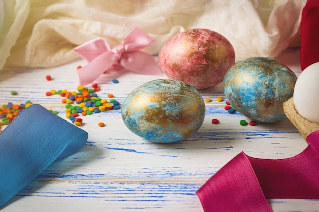 Huevos de Pascua, dulces, cintas en la mesa de madera blanca