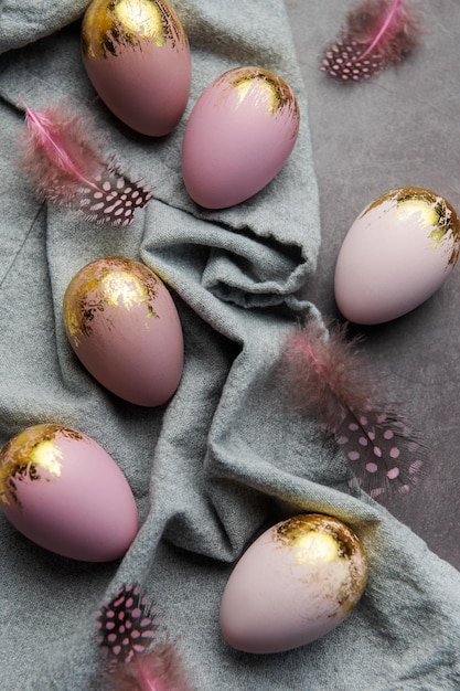 Los huevos de pascua están pintados con pintura violeta y dorada sobre un fondo de lino gris