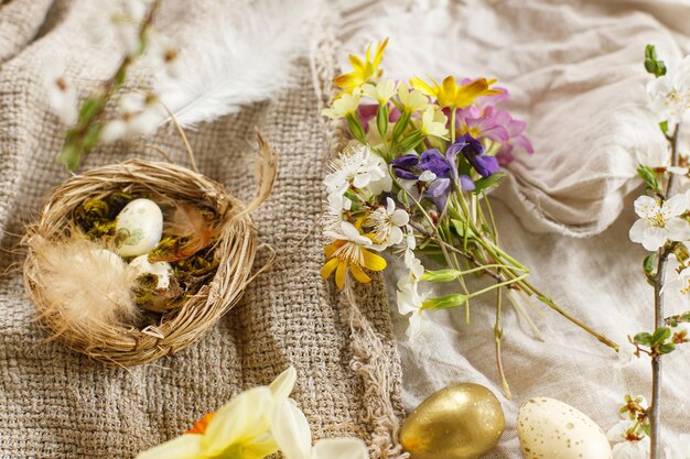 Huevos de Pascua con estilo y flores de primavera en flor sobre fondo de tela de lino Felices Pascuas Bodegón rústico de Pascua Huevos modernos en nido y flores silvestres