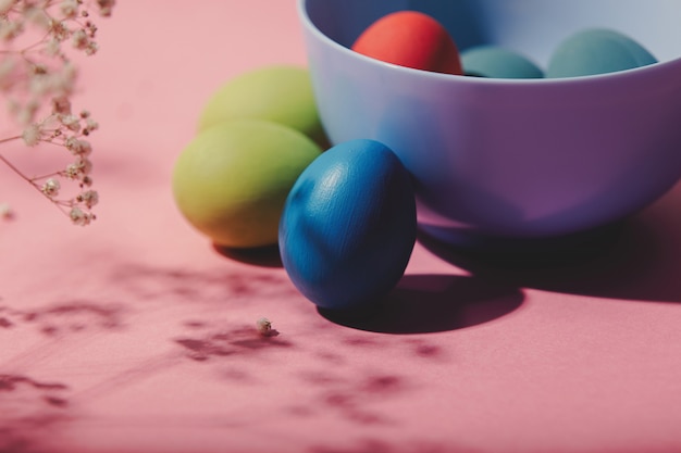 Huevos de Pascua, flores y plato sobre fondo rosa