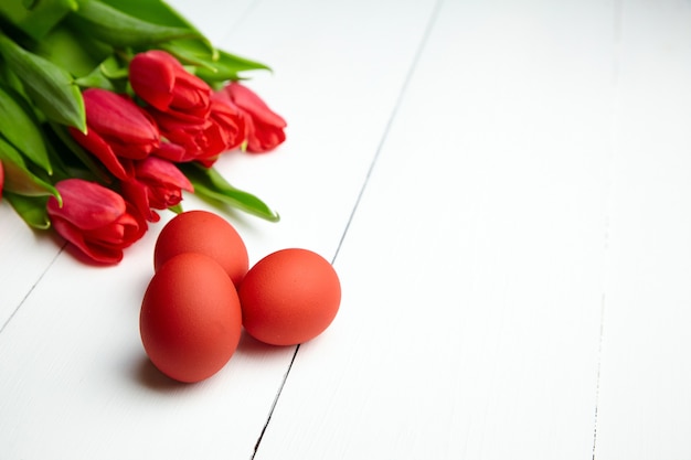 Huevos de Pascua y flores de tulipán rojo sobre mesa de madera blanca con espacio de copia