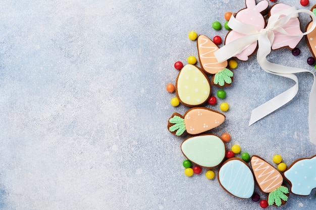 Huevos de Pascua, galletas y dulces coloridos en forma de corona circular sobre mesa gris. Concepto de vacaciones mínimo con espacio de copia de texto. Endecha plana