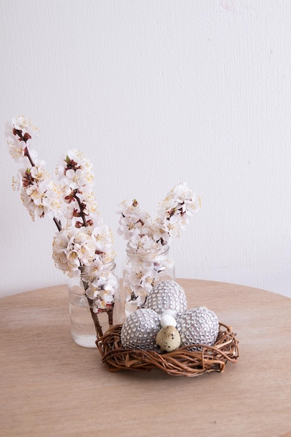 Huevos de Pascua glamorosos en un nido con flores. Decoraciones de mesa minimalistas en casa para las vacaciones de primavera.