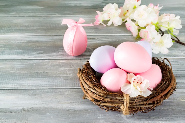 Foto huevos de pascua hechos a mano coloridos perfectos en un nido con flores de primavera en una pared gris de madera. felices pascuas