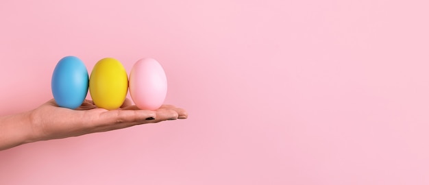 Huevos de Pascua en mano sobre fondo rosa, concepto de feliz Pascua, maqueta panorámica con espacio para texto