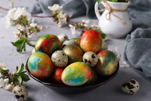 Huevos de Pascua de mármol pintados con colorantes alimentarios multicolores y huevos de codorniz en un plato sobre una superficie gris