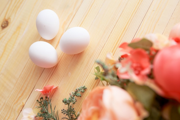 Huevos de Pascua en mesa de madera blanca. Flores y dulces alrededor.