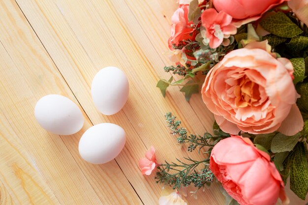 Huevos de Pascua en mesa de madera blanca. Flores y dulces alrededor.